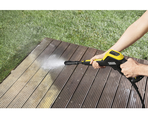 O persoană curăță o terasă din lemn cu un aparat de curățat cu presiune Kärcher.