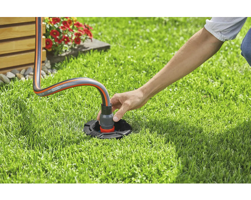 O persoană conectează un furtun de grădină la o priză de apă în grădină
