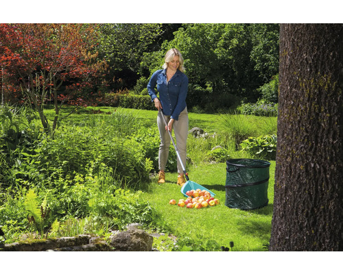 Femeie adunând mere cu un culegător de fructe într-o grădină