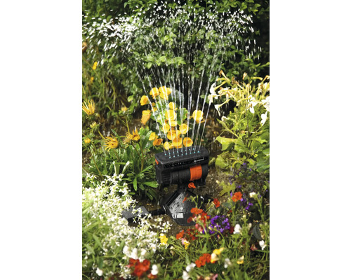 Aspersor oscilant în uz printre flori și plante