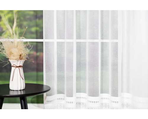 Cortină decorativă albă în fața unei ferestre, lângă o masă cu vază și flori uscate