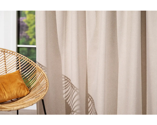 Cortină decorativă lângă un fotoliu de răchită cu pernă în fața ferestrei