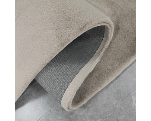 Vizualizare detaliată a unui covor bej cu un colț ondulat, care arată textura și partea inferioară