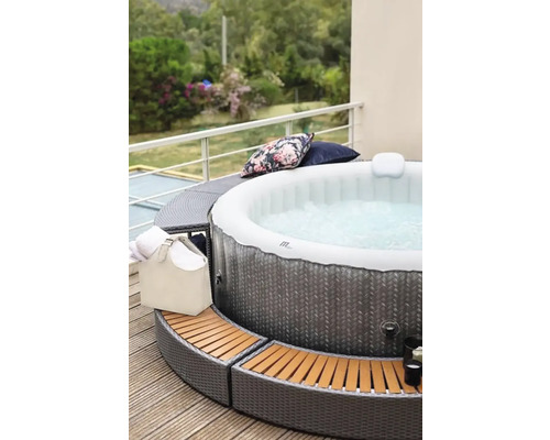 Jacuzzi gonflabil cu margine din ratan pe o terasă cu perne și prosoape