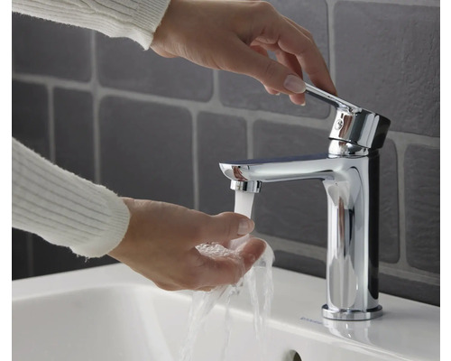 Persoană care se spală pe mâini sub un robinet cromat într-o chiuvetă