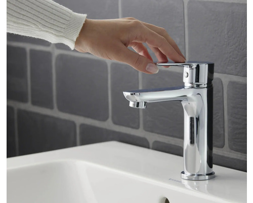 Mână care acționează robinetul pe o chiuvetă în baie.