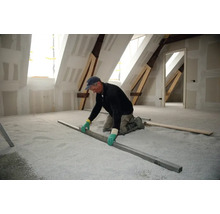 Un meșter nivelează materialul de umplere egalizator într-un pod cu o șipcă.