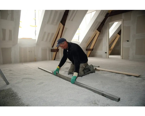 Un meșter nivelează materialul de umplere egalizator într-un pod cu o șipcă.