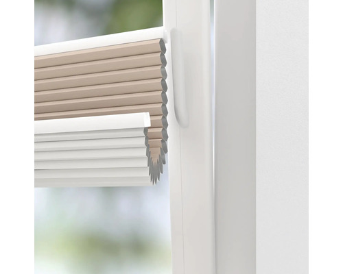 Prim-plan cu un jaluzea plisantă bej și albă la o fereastră