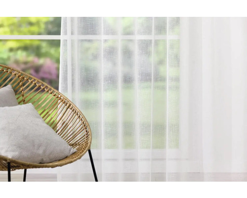 Cameră luminoasă cu fereastră, perdea transparentă și fotoliu de răchită cu perne