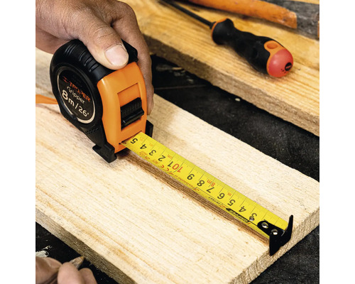 Mână ținând o ruletă Truper Gripper de 8 metri pe o scândură de lemn