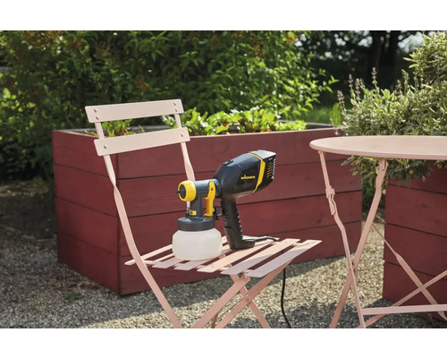 Sistem de pulverizare vopsea Wagner pe un scaun de grădină lângă o masă și un strat de flori înălțat