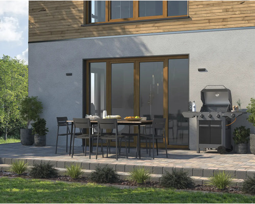 Terasa cu masă de grădină, scaune și grătar în fața unei case.