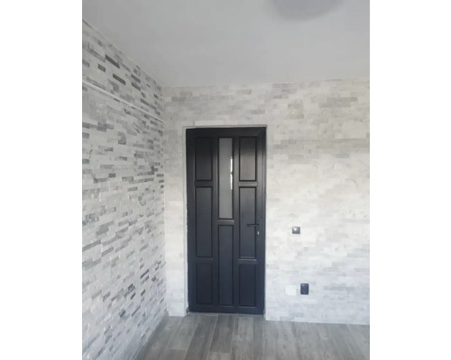 Ușă de interior cu inserție de sticlă într-o cameră cu un perete de piatră.