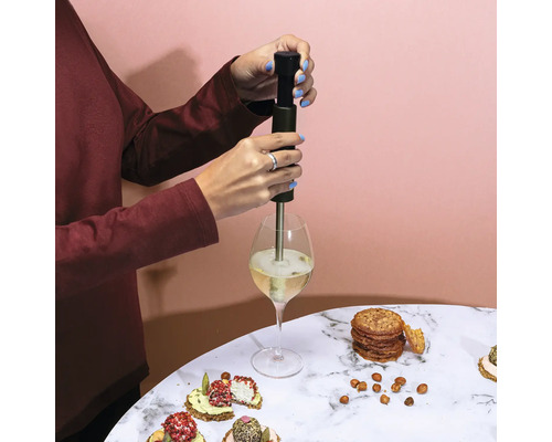 O persoană folosește un spumant de băuturi într-un pahar de vin, înconjurat de biscuiți și gustări pe o masă.