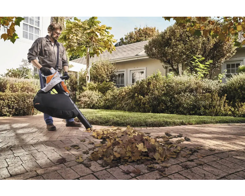 Un bărbat folosește un aspirator de frunze Stihl în grădină pentru a îndepărta frunzele.