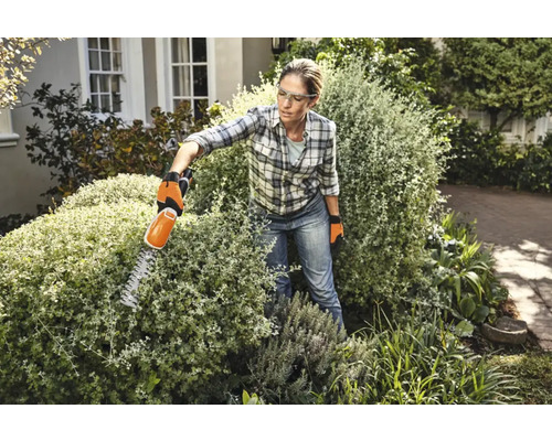 Femeie tăind un gard viu cu o foarfecă de gard viu în grădină.