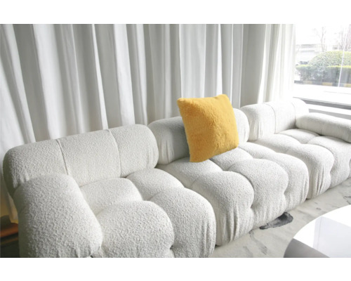 Canapea modulară cu pernă galbenă în fața unei ferestre cu perdele.