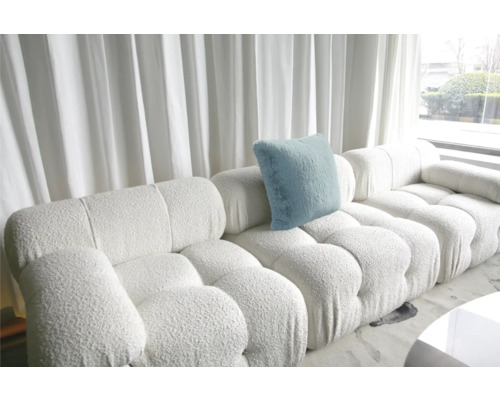 Canapea modulară albă cu pernă albastră deschisă în fața ferestrelor cu perdele