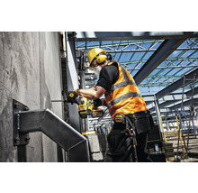 Un muncitor în construcții forează o gaură într-un perete pe un șantier cu un ciocan rotopercutor cu acumulator. Poartă echipament de protecție, iar ciocanul rotopercutor este de la DeWalt.
