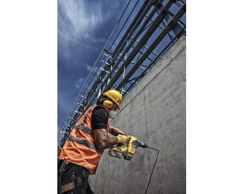 Muncitor în construcții care forează o gaură într-un perete de beton cu un ciocan rotopercutor.