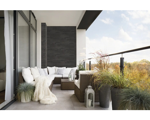 Balcon cu canapea din ratan, perne, pătură, felinare și ierburi ornamentale în ghivece.