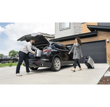 Un bărbat pune valize în portbagajul unei mașini, în timp ce o femeie trage un generator electric portabil pe roți.