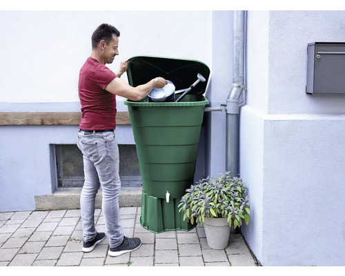 Bărbat umplând un butoi cu apă de ploaie cu o stropitoare și o găleată.