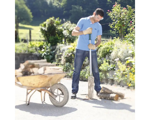 Un bărbat taie lemne cu un despicător de lemne lângă o roabă într-o grădină.