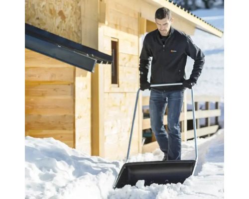 Bărbat care împinge zăpada cu o lopată de zăpadă în fața unei case de lemn