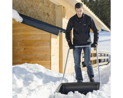 O persoană împinge zăpada cu o lopată de zăpadă în fața unei case din lemn.