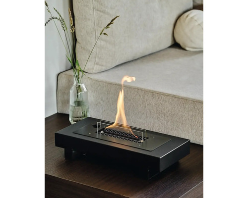 Șemineu cu etanol în negru pe o masă, lângă o canapea și o vază cu ierburi.