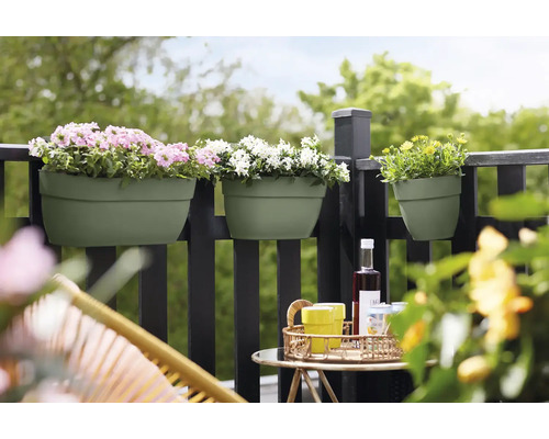 Scenă de balcon cu jardiniere pe o balustradă, plantate cu flori roz, albe și galbene, cu o masă și scaune în prim plan