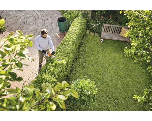 Un bărbat taie un gard viu cu o foarfecă de tuns gardul viu în grădină.