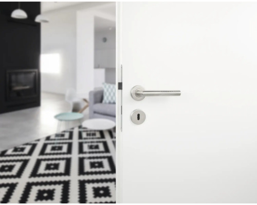 Ușă albă deschisă cu mâner din oțel inoxidabil spre o cameră de zi cu covor