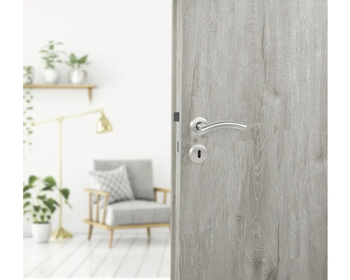 Ușă de lemn deschisă la culoare cu mâner argintiu într-o cameră luminoasă