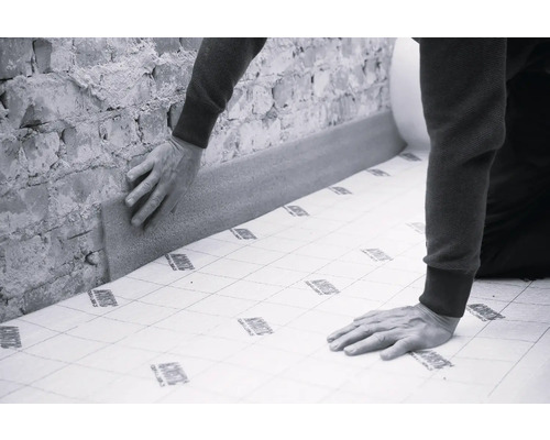 O persoană instalează izolație fonică pe un perete de cărămidă.