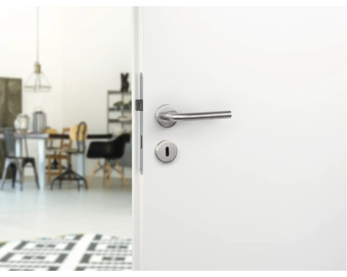 Ușă albă deschisă cu clanță argintie și vedere spre o cameră luminoasă