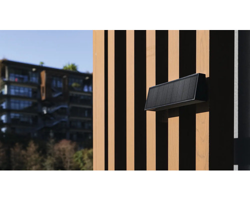 O lampă de perete neagră pentru exterior pe o fațadă din lemn.