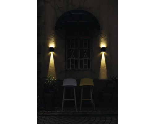 Exteriorul unei clădiri cu două scaune de bar sub o fereastră cu două aplice de perete.