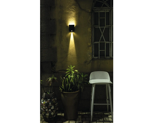 Scenă cu lampă de perete exterioară, ghivece de flori și scaun în grădină