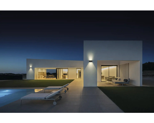 Fațadă modernă de casă cu iluminat exterior, piscină și șezlonguri la amurg.