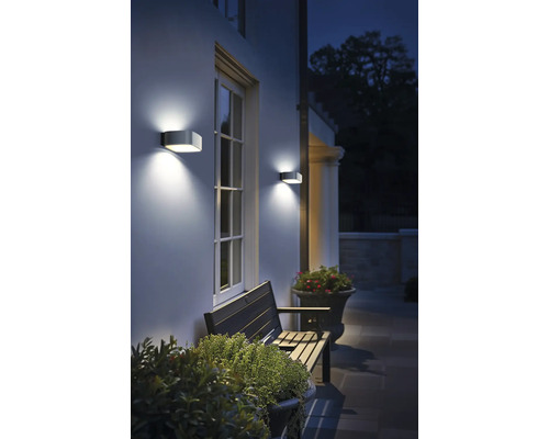 Scenă exterioară cu perete de casă, fereastră, bancă și două lămpi de perete.