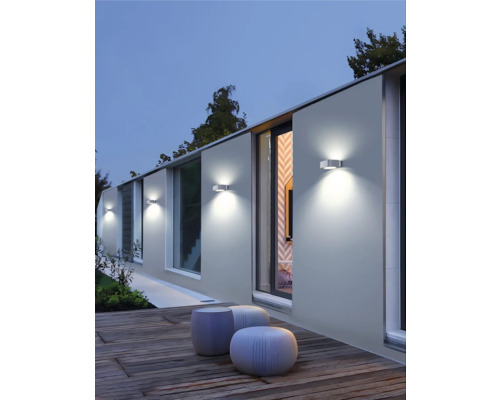 Perete de casă iluminat cu corpuri de iluminat exterioare și locuri de ședere pe o terasă de lemn.