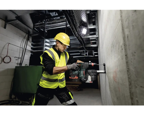 Un bărbat găurește cu un ciocan rotopercutor o gaură într-un perete de beton pe un șantier.