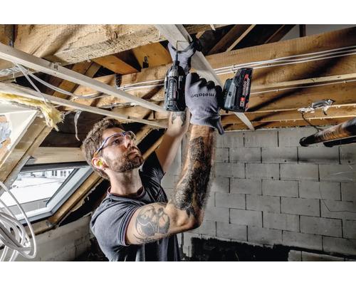 Un meșter lucrează cu o șurubelniță cu acumulator la o structură din lemn, purtând ochelari de protecție și protecție auditivă.