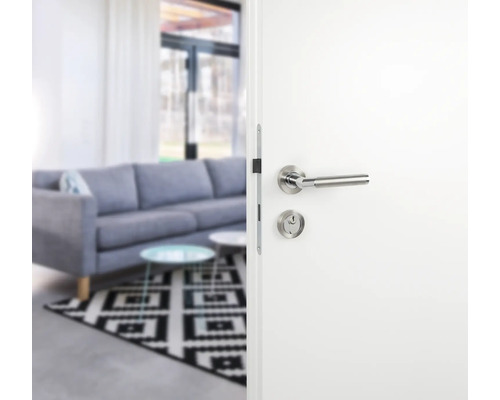 Ușă interioară albă deschisă, cu feronerie, în fața unui spațiu de locuit