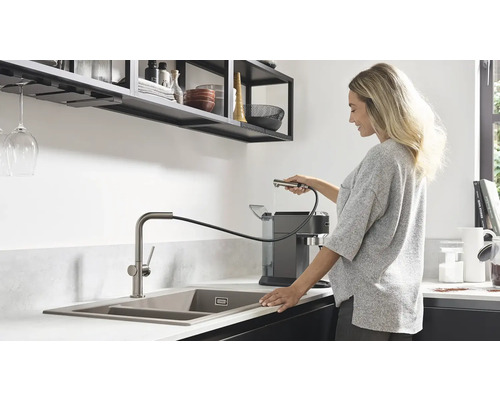 Bucătărie modernă cu chiuvetă, baterie cu duș extractibil și femeie care umple o mașină de cafea.