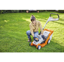 O femeie introduce o baterie într-o mașină de tuns iarba Stihl în grădină.