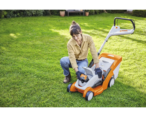 O femeie introduce o baterie într-o mașină de tuns iarba Stihl în grădină.